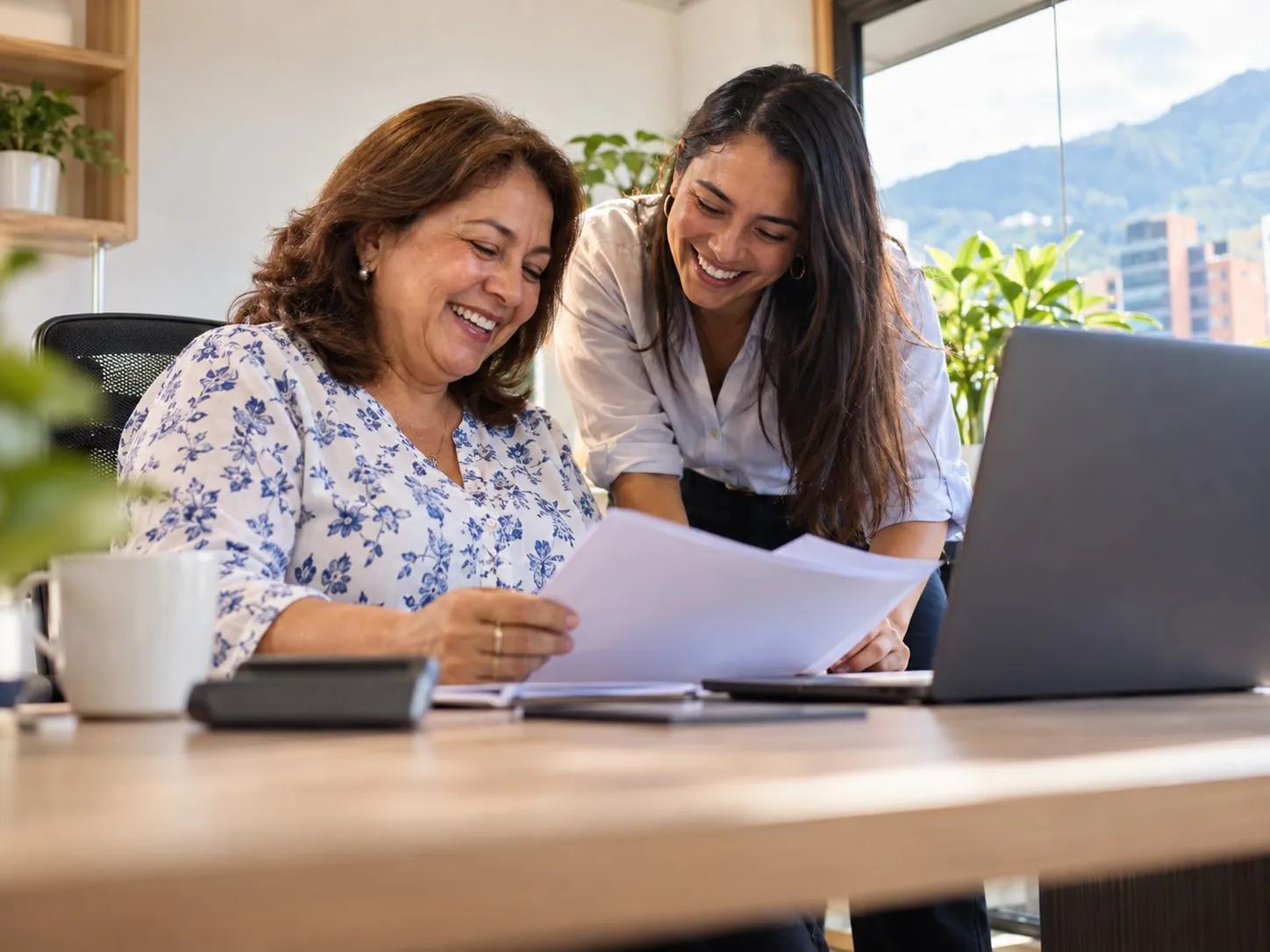 Una contadora y su colega se ríen mientras revisan unas hojas en una oficina